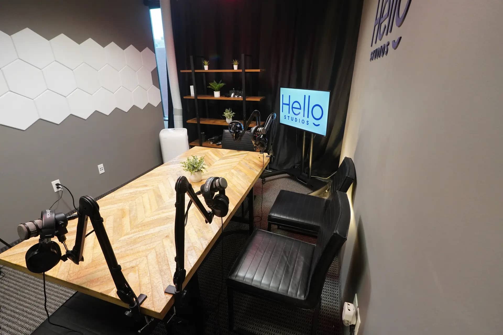 The Iron flagship suite: a herringbone table, broadcast microphones, a hexagon acoustic wall, and the Hello Studios screen.