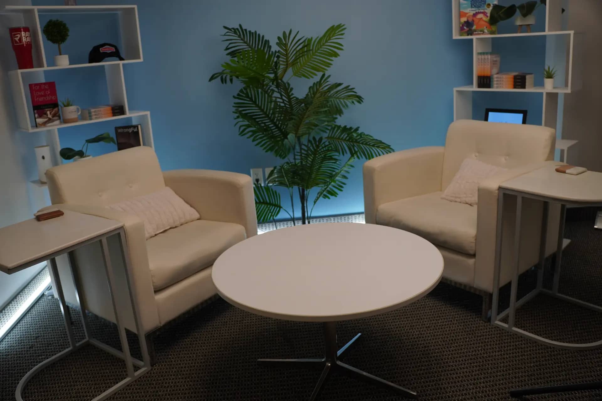 The Opal lobby lounge: cream armchairs, a plant, and styled shelving against a blue accent wall in the Dallas podcast studio.