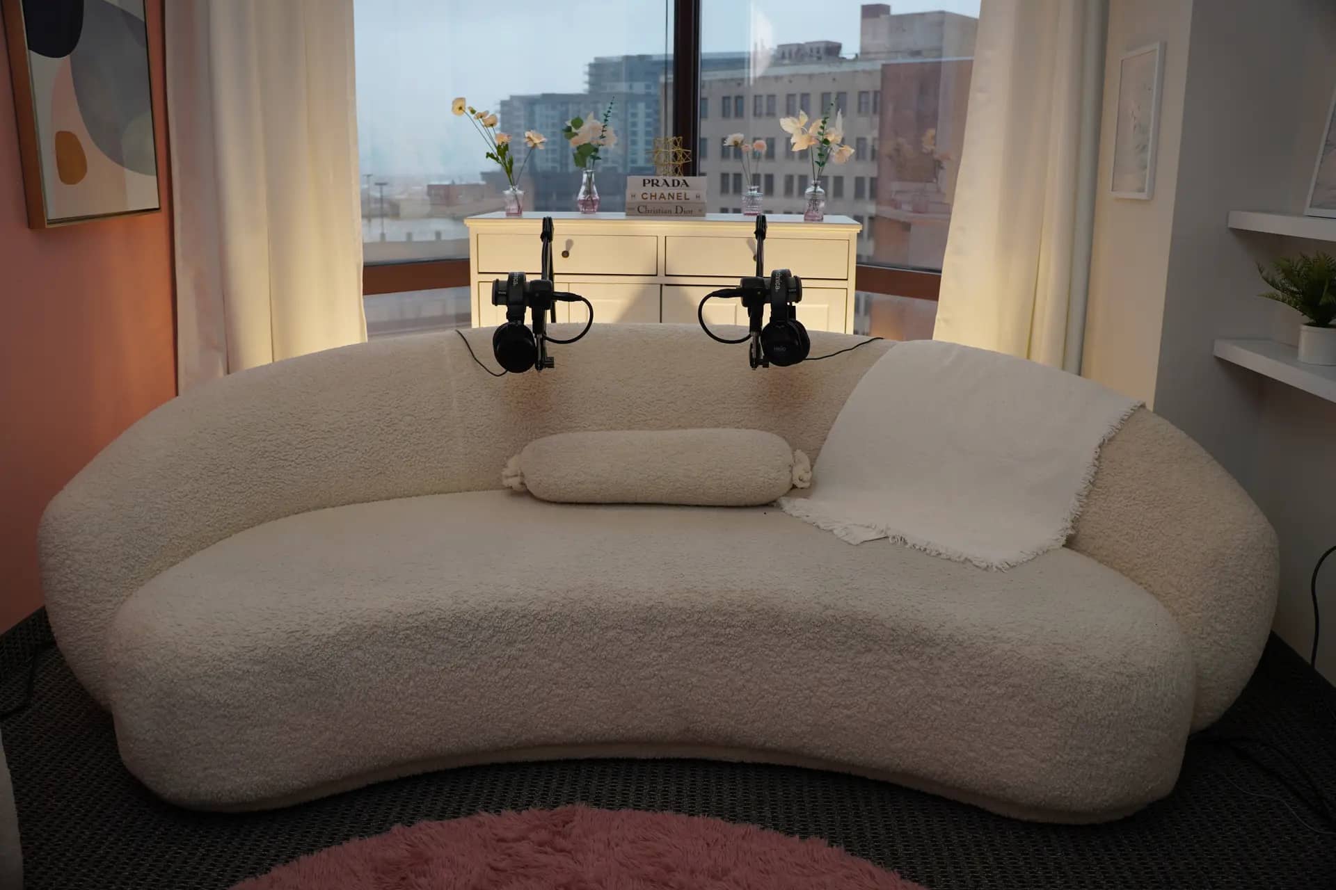 The Quartz daylight set: a curved cream bouclé sofa framed by a downtown Dallas skyline window, florals, and framed art.