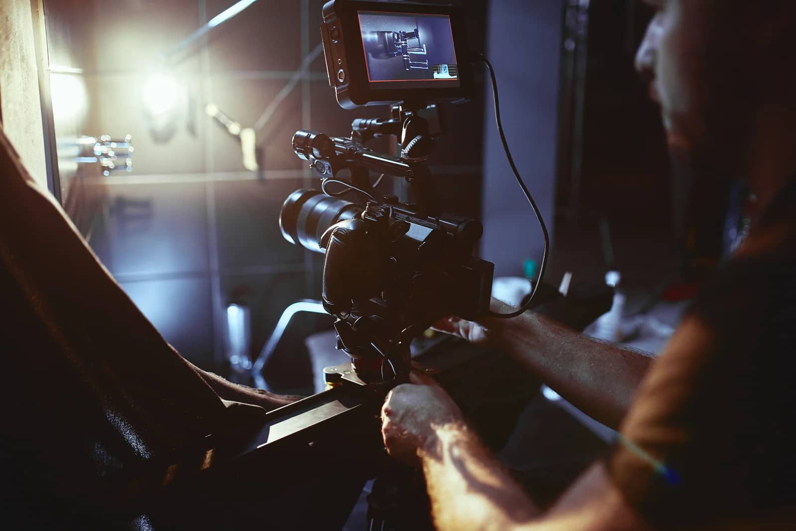 Camera operator's hands on a video camera rig, with the monitor on top showing the framed shot in a dim studio Camera operator's hands on a video camera rig, with the monitor on top showing the framed shot in a dim studio