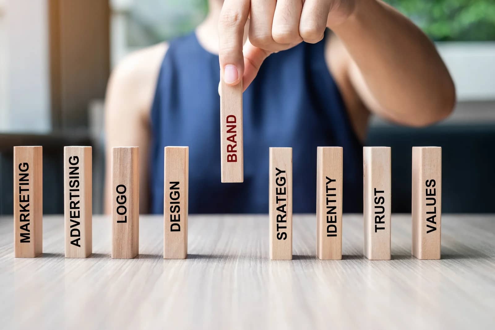 Hand lifting a wooden block labelled BRAND from a row of blocks marked marketing, logo, design, strategy, identity, trust and values Hand lifting a wooden block labelled BRAND from a row of blocks marked marketing, logo, design, strategy, identity, trust and values