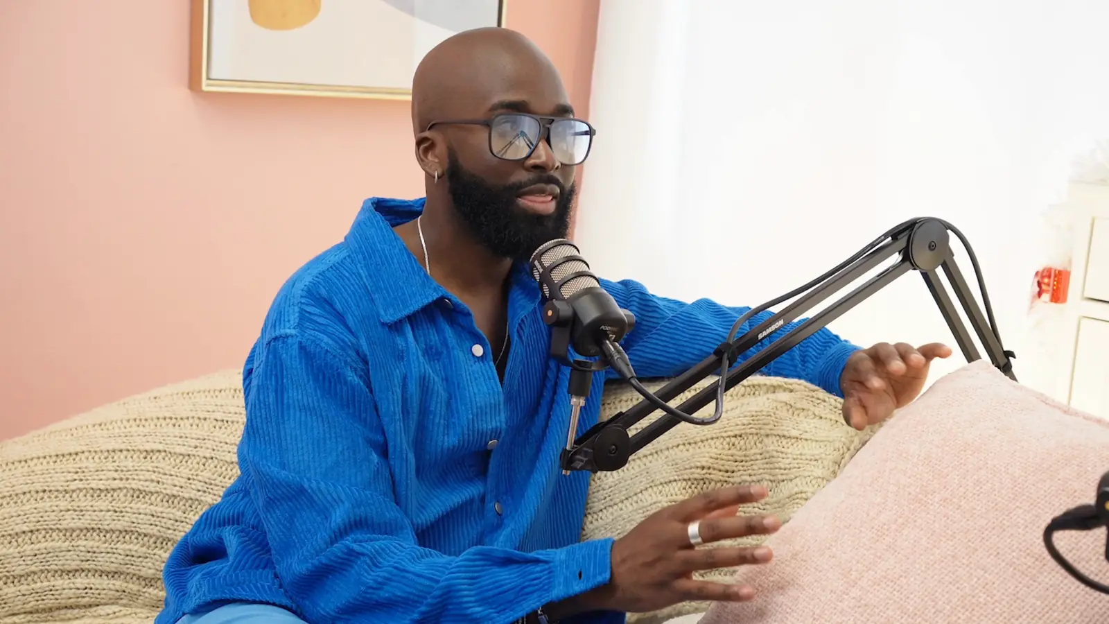 A partner recording an episode A man in a blue shirt speaking into a broadcast microphone on a boom arm during a podcast recording.