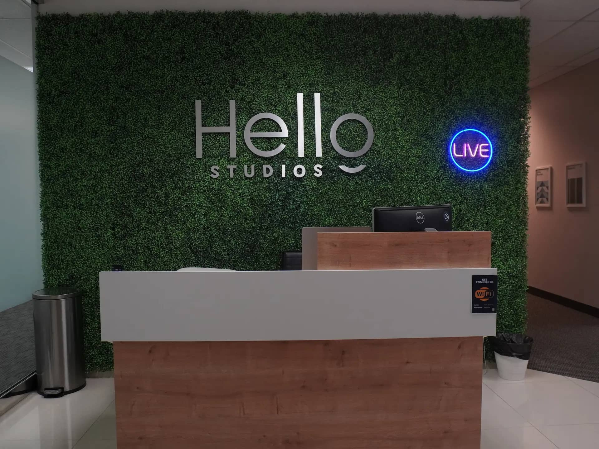 The reception desk and living-greenery Hello Studios wall inside the Sierra Media Productions Dallas podcast studio.