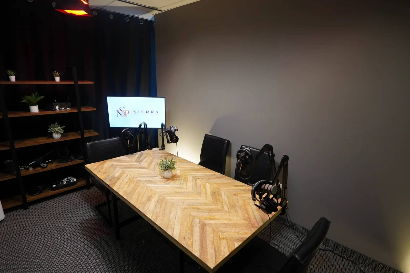 Podcast recording suite, seating and lighting The same recording suite from the doorway, showing black leather chairs at the table, shelving, and a screen showing the Sierra Media Productions logo.
