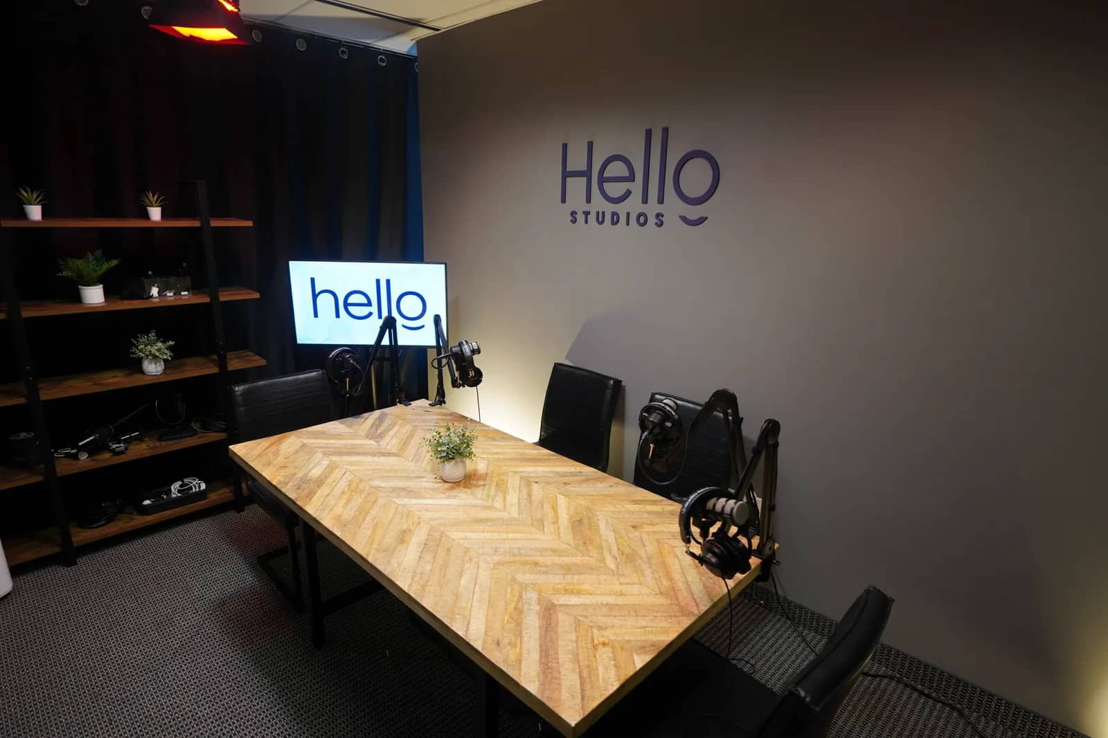 Podcast recording suite, seating and lighting The same recording suite from the doorway, showing black leather chairs at the table, shelving, and an illuminated Hello Studios light box.