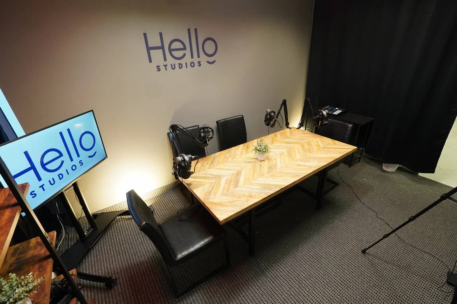 Podcast recording room, wide view A wider view of the recording room with acoustic drapery, a lighting stand, boom microphones and the Hello Studios wall mark.